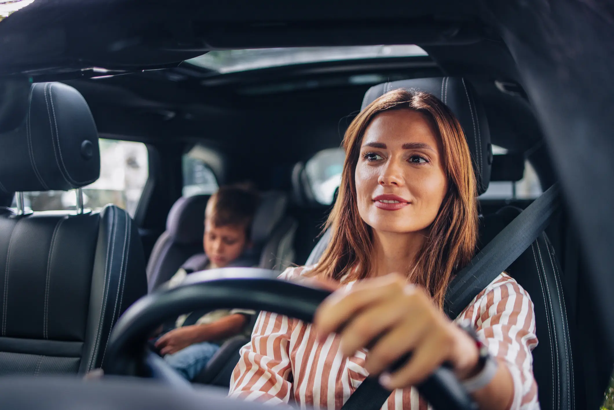 A woman driving a car with a child in the backseat.