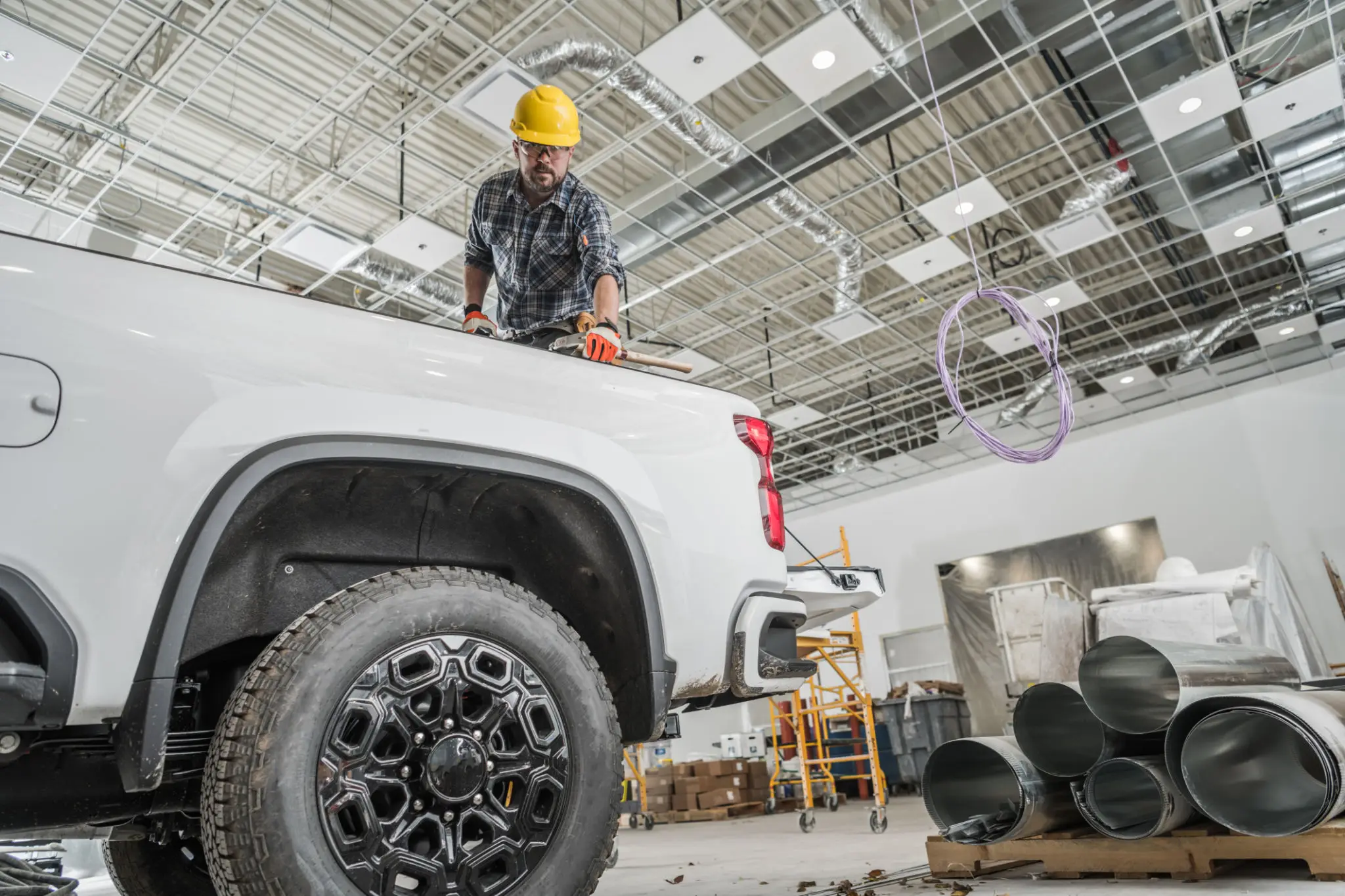 Worker in safety gear inspecting a white pickup truck in a workshop.