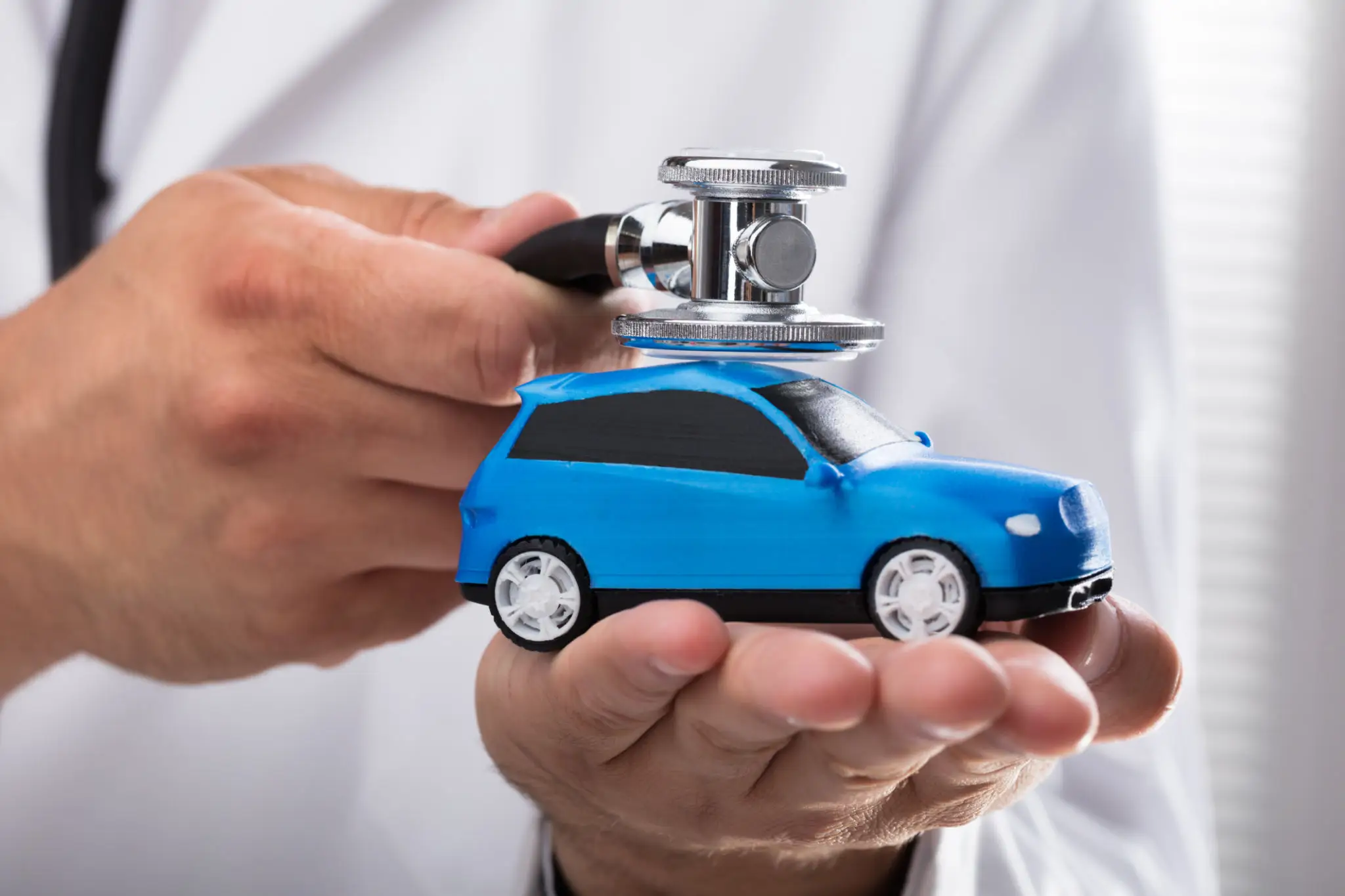 Hand holding a small blue toy car with a stethoscope on top.